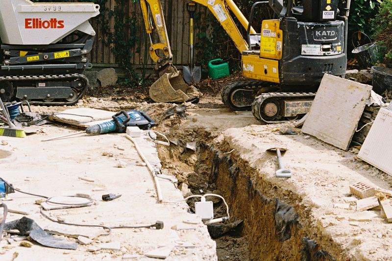 Mini excavator and dumper beside an excavation trench next to a house